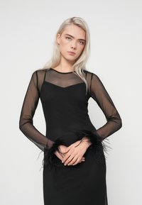 Vestido preto de manga longa com tecido de malha transparente, silhueta justa e detalhes de penas nas mangas. Textura suave em toda a peça.