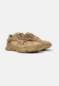 Sandfarbene Wildleder-Sneaker mit strukturiertem Finish, gepolstertem Zungenbereich, flachen Schnürsenkeln und einer klobigen Gummisohle, die minimale Markenkennzeichnung an den Seiten aufweist.