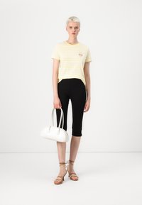 Gulrandig t-shirt med ett litet broderat mönster, kombinerad med svarta capri-leggings, bruna sandaletter med remmar och en vit handväska.