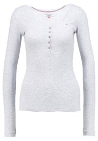 Maglietta grigia a maniche lunghe con scollatura a V, texture a coste e chiusura frontale con sei bottoni. Presenta cuciture di accento rosse sottili.