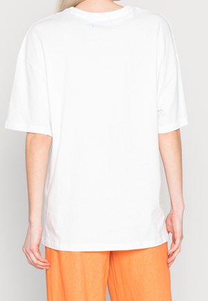 Camiseta blanca de gran tamaño con cuello redondo y hombros caídos, fabricada en suave tela de algodón. La vista trasera muestra un diseño sin adornos.