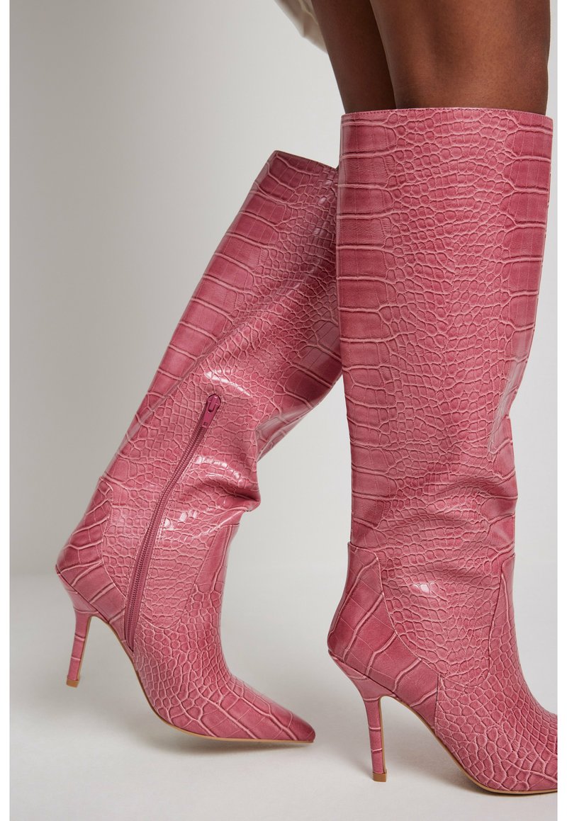 Bottes montantes en cuir synthétique rose brillant avec une texture crocodile, bout pointu et talon stiletto effilé ; doté d'une fermeture éclair latérale.