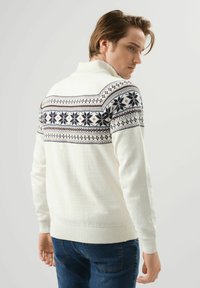 Biały sweter dzianinowy z wysokim kołnierzem, z wzorzystym wzorem w granatowym i brązowym kolorze na ramionach. Prążkowane mankiety i dół.