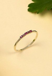 Guldring med fem rosa ädelstenar inställda i en krökt rad längs med bandet, med en slät, polerad yta.