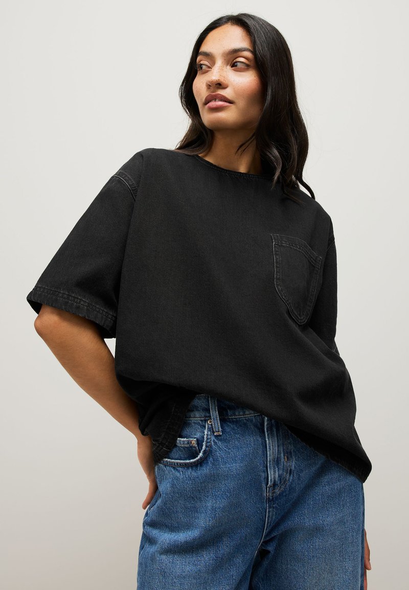 T-shirt noir surdimensionné à manches courtes, col rond et poche poitrine, assorti à un jean en denim bleu. La texture semble lisse.