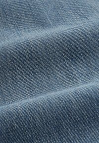 Gros plan sur un tissu en jean bleu texturé avec un tissage diagonal visible et des variations subtiles de couleur et d'ombrage.