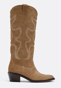 Botte cowboy en daim beige mi-mollet avec motifs ondulés cousus, languette de tirage, bout pointu et talon en bois empilé incliné.