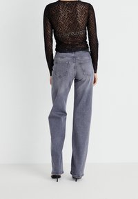 Svart leopardmönstrad långärmad topp som matchas med högmidjade, ljusgrå raka jeans med bakfickor och en klassisk denimtextur.