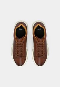 Καφέ δερμάτινα αθλητικά παπούτσια με λεία υφή, λευκές καουτσούκ σόλες και εσωτερική επένδυση σε αντίθετη ταμπά απόχρωση. Διαθέτουν σχέδιο με κορδόνια και λογότυπο.