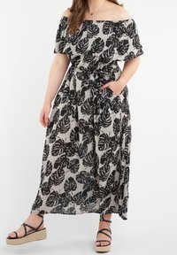 Mustavalkoinen olkapäiltä avoin maksimekko, jossa on lehväkuvio, vyötäröltä kiristetty malli ja sivutaskut, yhdistettynä mustiin hihna-ankkureihin.