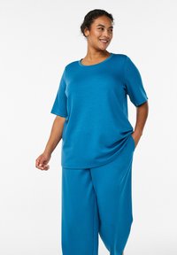 Türkisfarbenes Kurzarmshirt mit rundem Ausschnitt, kombiniert mit passenden weit geschnittenen Hosen. Der Stoff ist glatt mit leichtem Glanz; legerer Schnitt.