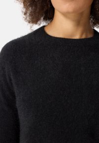 Svart ulltröja med runt halsringning och mjuk, fluffig textur, synlig runt axelområdet.