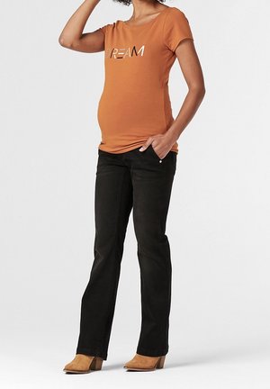 Camisa de maternidad naranja de manga corta con la palabra "DREAM" impresa en un estilo reflectante, combinada con jeans negros de pierna recta y botas de tacón en color beige.