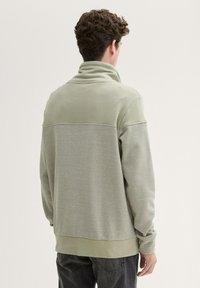 Pullover in felpa di colore verde chiaro con colletto alto, caratterizzato da una parte superiore testurizzata e un motivo a strisce contrastanti nella sezione inferiore.