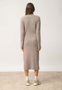 Abito lungo a coste color beige chiaro, realizzato in un materiale morbido. Presenta un colletto alto e una silhouette aderente con polsini e orlo a coste.