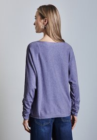 Maglia a maniche lunghe viola con una vestibilità ampia, tessuto testurizzato, spalle scese e polsini arrotolati, abbinata a jeans blu scuro.
