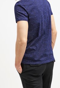 Camiseta de manga corta en color navy con un patrón geométrico en diferentes tonalidades de azul, fabricada en tejido suave; cuenta con un escote redondo y una silueta ajustada.