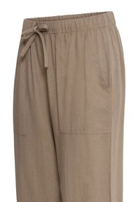 Luźne, jasnobrązowe spodnie z elastycznym pasem i sznurkiem, wyposażone w przednie naszywane kieszenie.