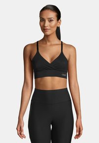Sujetador deportivo negro con un diseño en forma de V y tirantes finos, que presenta una textura suave y un detalle de logo en la banda, combinado con mallas negras.