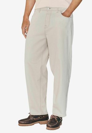 Pantalones sueltos de color beige claro, con piernas rectas, un diseño clásico de cinco bolsillos y costuras de contraste. Combinados con zapatos marrones.