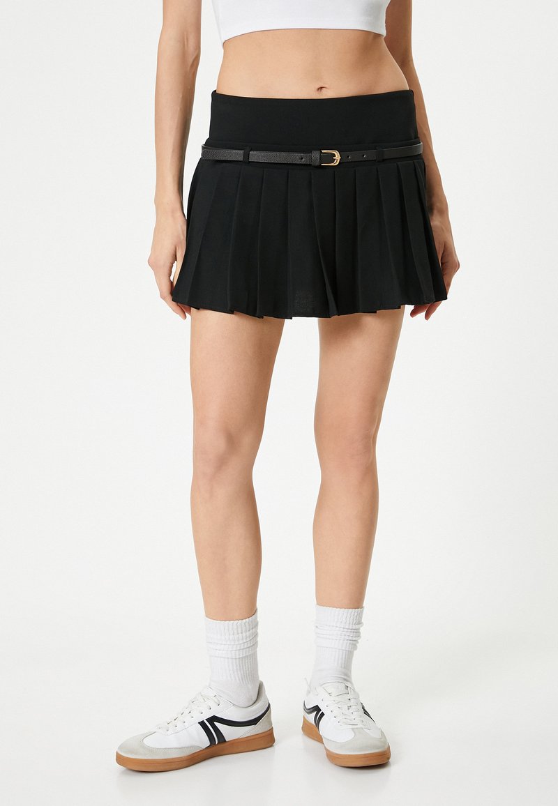 Mustat laskostetut hameet korkealla vyötäröllä, kultakuljettimella varustettu vyö. Yhdistettyinä valkoisiin lenkkikenkiin ja teksturoituihin sukkiin.