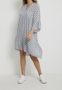 Lätt, knä-length klänning med V-ringning, ballongärmar, blå och vit scallop-mönster och rynkad midja. Bärs med vita sneakers.