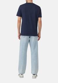 Marineblauwe katoenen T-shirt met korte mouwen en een klassieke ronde hals, gedragen met lichtblauwe wijde jeans en witte sneakers.
