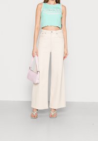 Mintgrön cropped tanktop med scalloped fåll, ljusbeige vida jeans, pastellrosa handväska och teal sandaler. Släta tygtexturer.