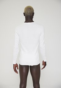 Hvid langærmet skjorte med en tætsiddende design, der viser en glat tekstur, rund halsudskæring og minimal detaljer.