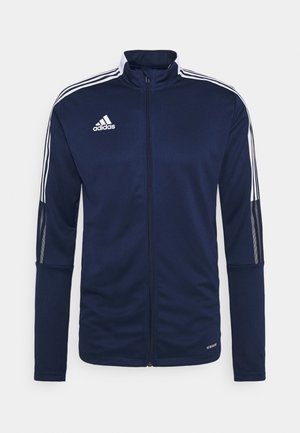 Dunkelblaue Sportjacke mit weißen Streifen auf Schultern und Ärmeln, hohem Kragen, durchgehendem Reißverschluss und dem "adidas"-Logo auf der oberen linken Brust.
