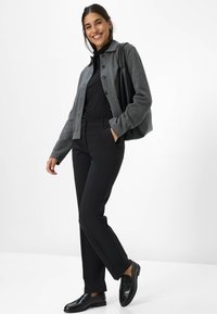 Grijze wolmix jas met knopen, zwarte coltrui, zwarte op maat gemaakte broek en zwarte loafers. Model met een zwarte schoudertas.