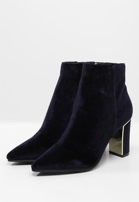Botas de tobillo de terciopelo azul marino con punta afilada y tacón cuadrado metálico. Textura lisa sin patrones visibles ni herrajes.