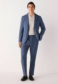 Blau strukturierte Anzugjacke und passende Hose kombiniert mit einem hellbeigen Poloshirt. Schwarze Dressschuhe. Minimalistisches Design, taillierte Silhouette.