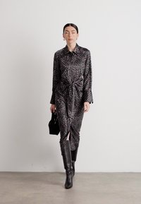 Abito leopardato in bianco e nero con cintura in vita, maniche lunghe e uno spacco frontale, abbinato a stivali neri al ginocchio e una piccola borsa nera.