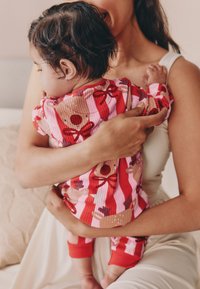 Ensemble de pyjama à rayures rouges et roses avec motifs festifs de rennes et de nœuds. Texture côtelée douce, accents rouges aux poignets et graphiques colorés.