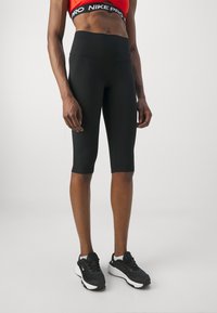 Mustad capri retuus, mis on valmistatud venivast materjalist, kõrge vöökoha ja kontrastsete õmblustega. Kantud mustade sportlike kingadega.