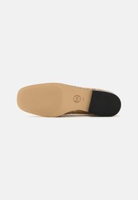 Chaussure pour femme avec une semelle plate en caoutchouc beige texturé et un talon noir. La tige présente un motif dans des tons terreux.