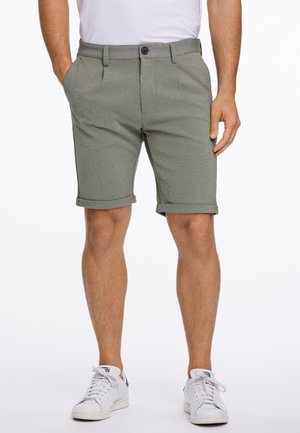 Shorts beige en tissu texturé, dotés d'une fermeture à bouton, de passants de ceinture et de revers roulés. Assortis à des baskets blanches.