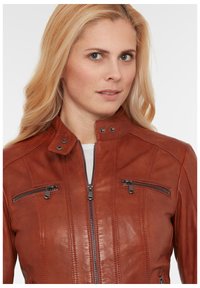 Braune Lederjacke mit hohem Kragen, zwei verschließbaren Taschen und strukturierten Details an den Schultern und vorne. Mit Reißverschluss.