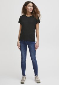 Černé tričko s krátkým rukávem a kulatým výstřihem, kombinované s modrými skinny džíny. Modelka má na sobě šedé sportovní tenisky. Pozadí je jednobarevné bílé.
