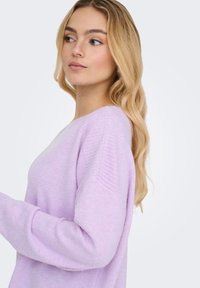 Jasnofioletowy sweter o luźnym kroju, z prążkowaną teksturą na ramionach i rękawach, wykonany z miękkiego dzianego materiału.