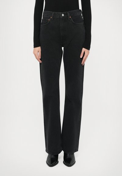 Jean noir taille haute avec coupe ample, design à cinq poches et coutures contrastantes subtiles. Porté avec des escarpins noirs à bout pointu.