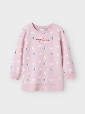 Rosa sweatshirt med vita och blå hjärtmotiv. Har ribbade muddar och fåll, rund halsringning och broderad text "stay kind."