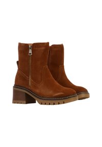 Stivaletti in suede marrone con tacco a blocco, cerniera laterale e dettagli di cucitura a contrasto lungo la suola. Suola di gomma testurizzata e robusta.