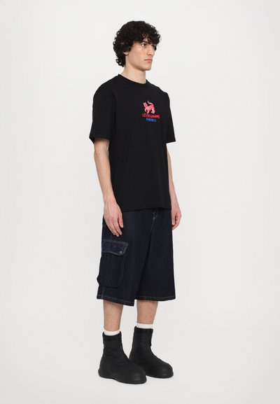 T-shirt noir à manches courtes avec un texte graphique rouge et bleu, associé à un short cargo en denim foncé avec des poches latérales et des bottines noires.