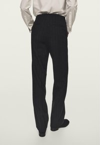 Černé kalhoty s jemným proužkem a rovnými nohavicemi, vyrobené z hladkého materiálu s upraveným střihem, viditelnými zadními kapsami a vysokým pasem.