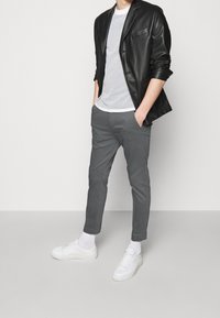 Zwarte leren blazer over een gestreept wit T-shirt, gecombineerd met grijze slim-fit broek en witte sneakers. Soepele texturen en een op maat gemaakte pasvorm.