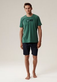 Zielony bawełniany t-shirt z grafiką "OFF", połączony z granatowymi szortami kąpielowymi w wzory, z elastycznym paskiem i sznurkiem do ściągania.