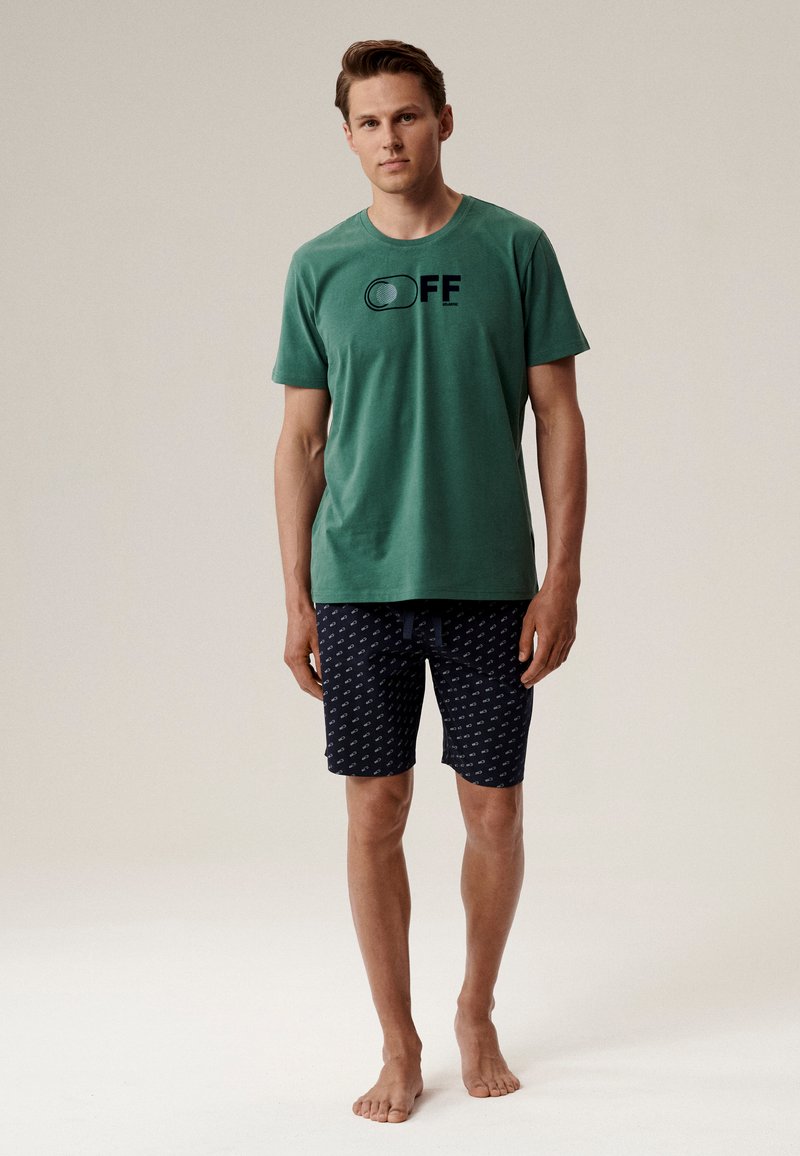 Zielony bawełniany t-shirt z grafiką "OFF", połączony z granatowymi szortami kąpielowymi w wzory, z elastycznym paskiem i sznurkiem do ściągania.