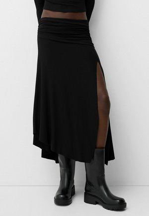 Black asymmetrical skirt with gathered waistband and side slit, paired with knee-high black leather boots, creating a sleek silhouette.